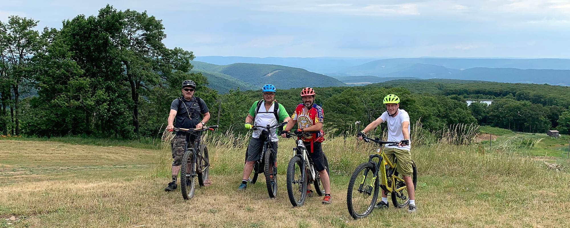 Mountain bikers stand on a grassy field atop a mountain