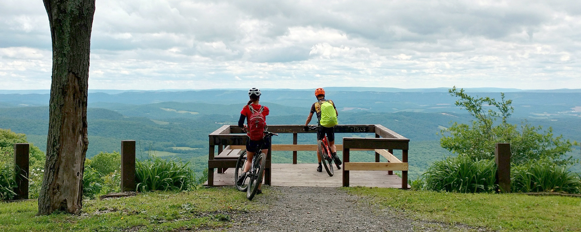 Two mountain bikers stand at a mountain overlook