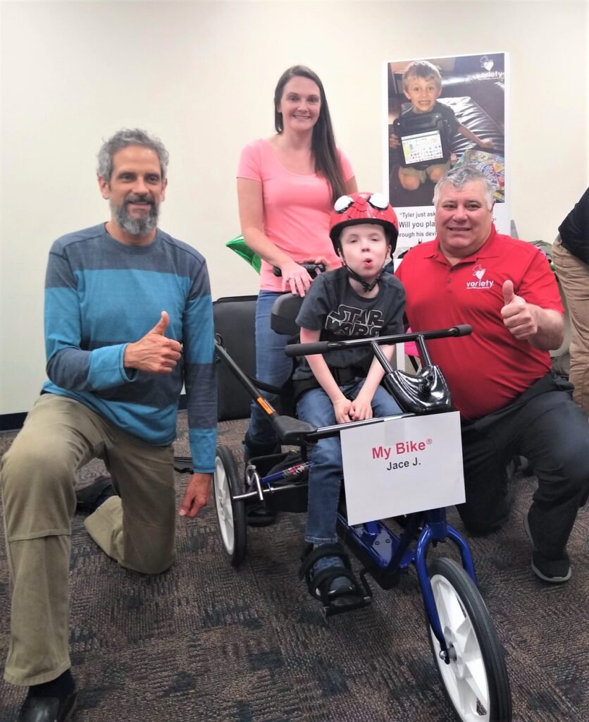 A child sits on a adaptive bike, surrounded by 3 adults